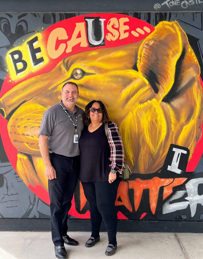 A man and woman standing in front of a mural.